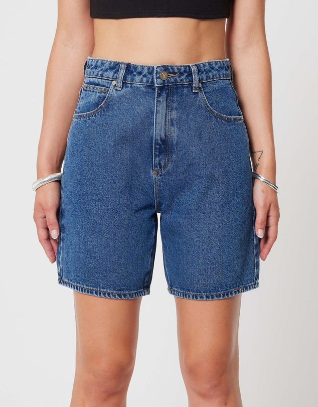 A pair of blue denim shorts with a high waist, viewed from the side with the wearer's back and arm visible.